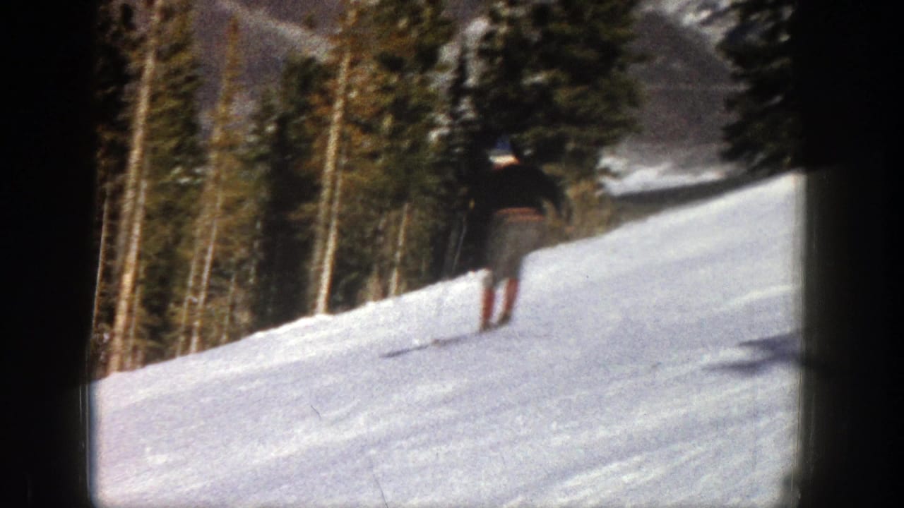 Distant skier moving downhill on a snowy slope bordered by evergreen trees.