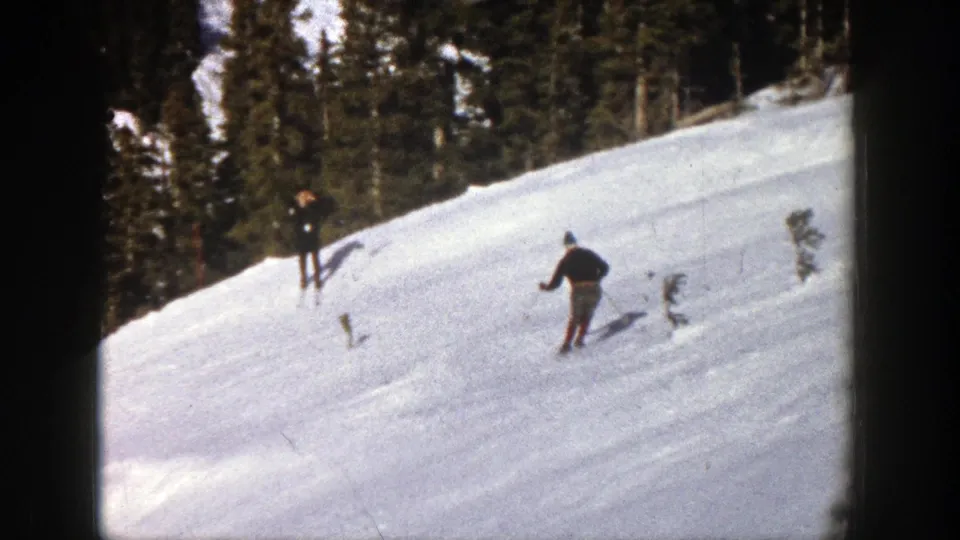 1961 Aspen home-movie frame showing a skier on a bright snowy slope below dark evergreen forest.