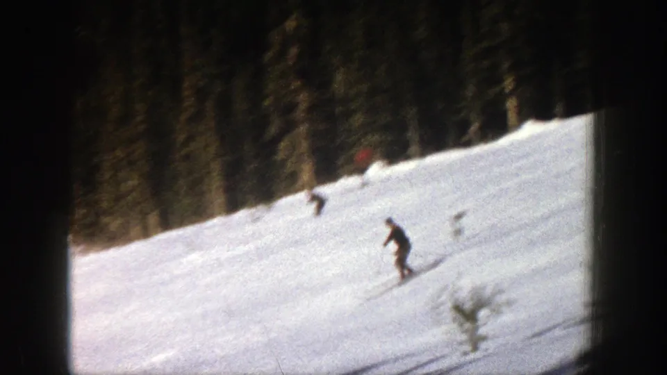 Two skiers are visible on a bright Aspen snow slope, one lower in frame and another near the trees.