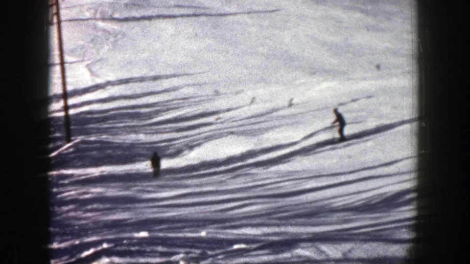 A distant skier crosses the lower part of the Aspen slope while shadows and ski tracks cut across the snow.