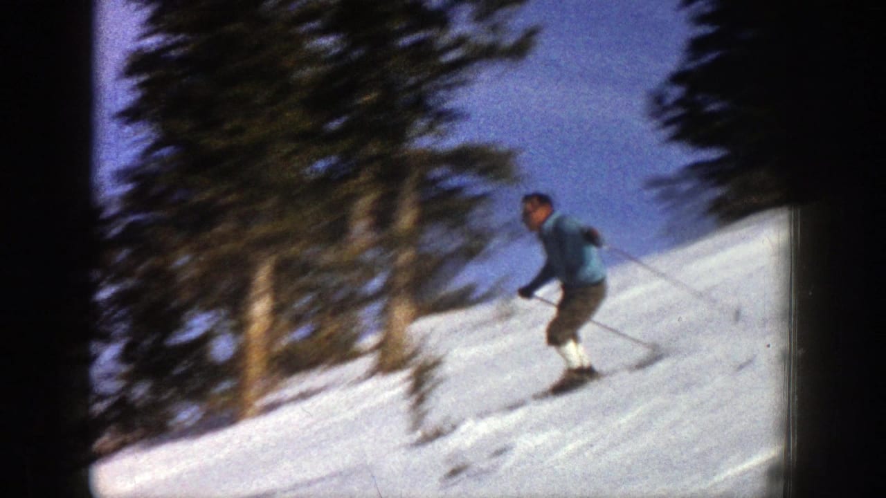 Skier in blue descending a bright snowy hillside with trees behind him.