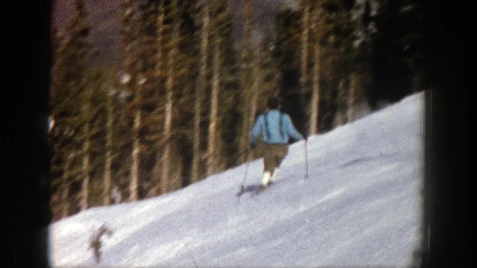 The skier moves away down the Aspen mountainside, passing a tree-lined section of the snowy slope.