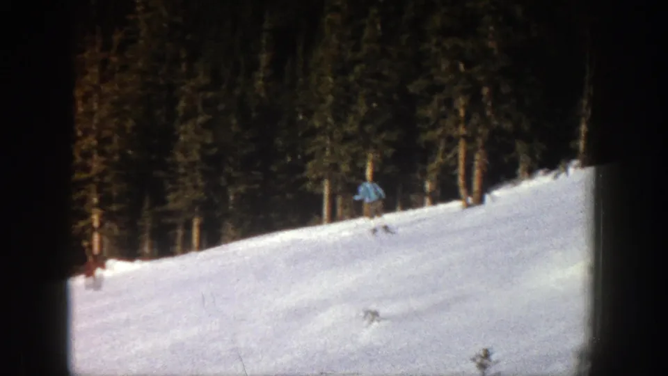 Near the end of the 1961 Aspen clip, the skier appears small against the snowfield, with evergreens filling the background.