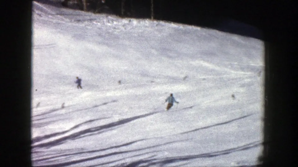1961 Aspen frame showing skiers spread across a wide snow-covered slope with long shadows and forested edges.