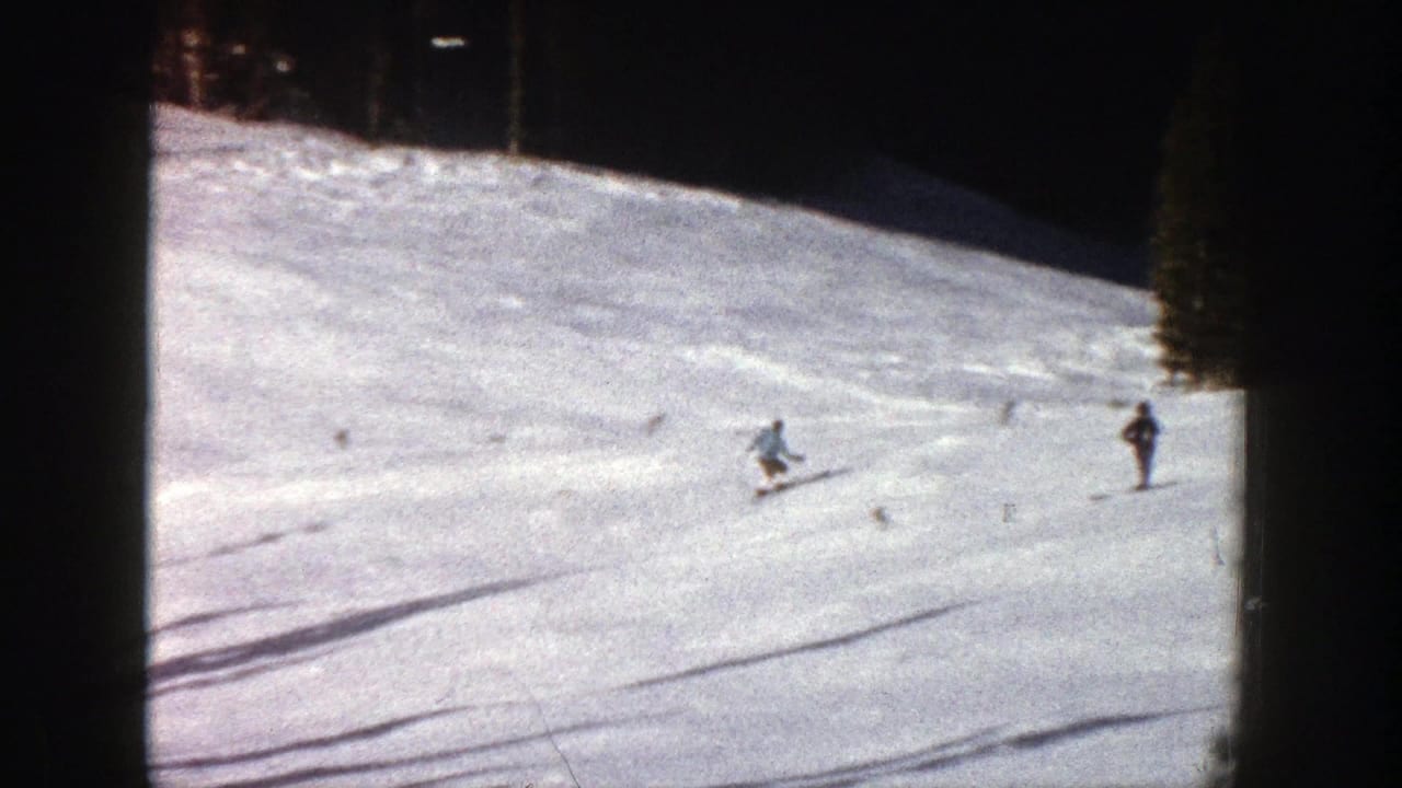 A skier turns across the slope while other skiers stand farther away.
