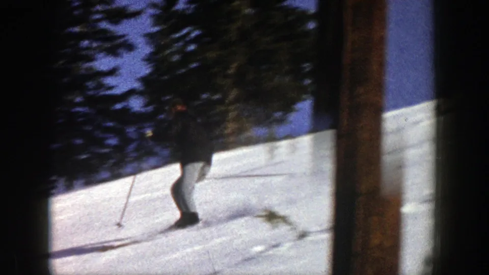 1961 Aspen frame with a nearby skier using poles on a sunlit snow slope, partly framed by dark film borders and trees.