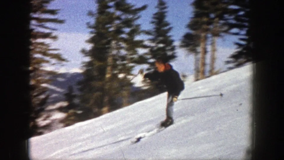 The skier continues downhill in Aspen, Colorado, framed by snow, pine trees and distant mountain terrain.