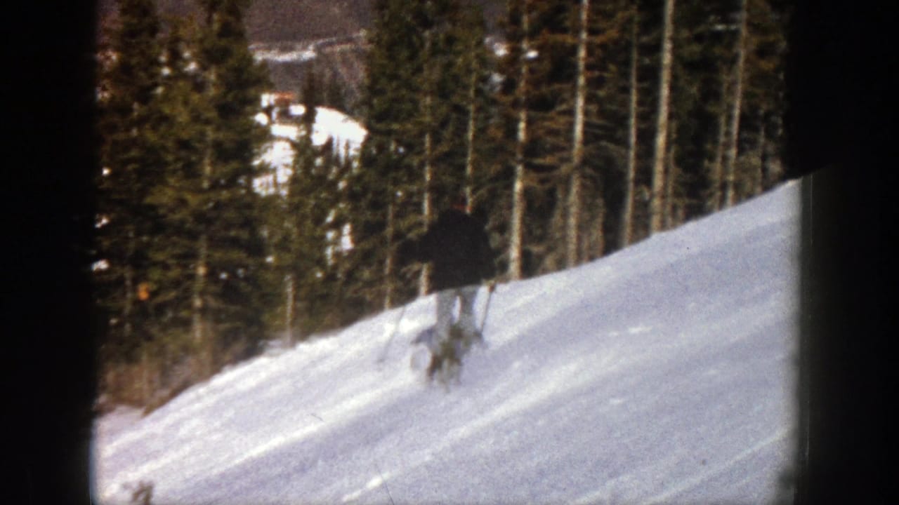 In metadata-supported 1961 Aspen, a lone skier in dark clothing crosses a gentle snow-covered slope near evergreens.