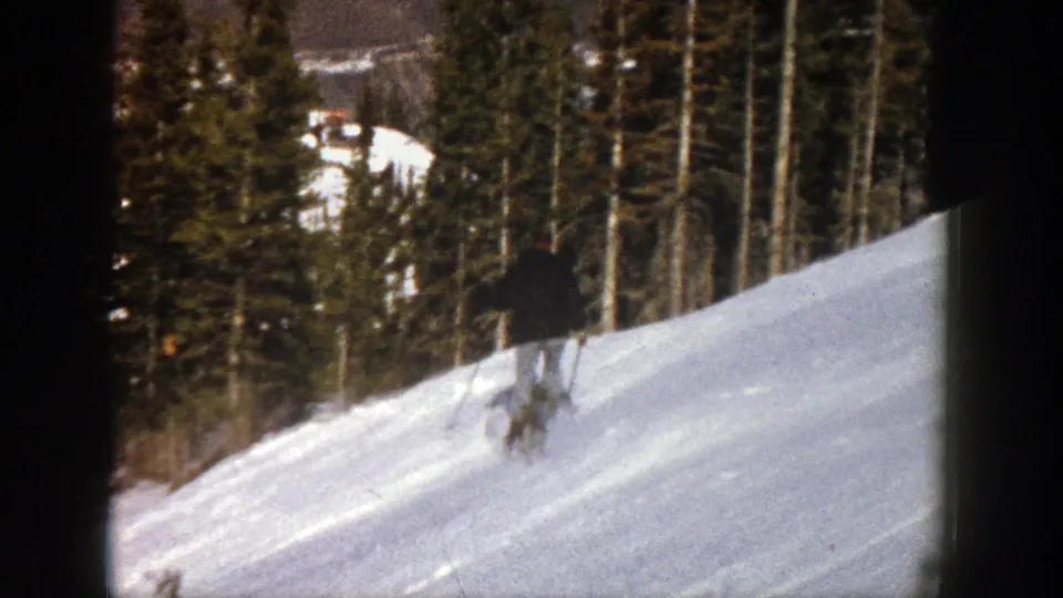 In metadata-supported 1961 Aspen, a lone skier in dark clothing crosses a gentle snow-covered slope near evergreens.
