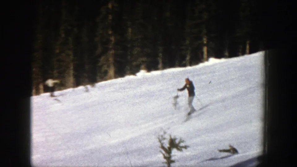 1961 Aspen home-movie still showing a skier descending a snowy slope, framed by heavy 8mm borders and a conifer backdrop.