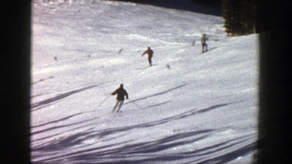 1961 Aspen home-movie frame showing several skiers spaced across a sunlit snowy slope with dark film borders.