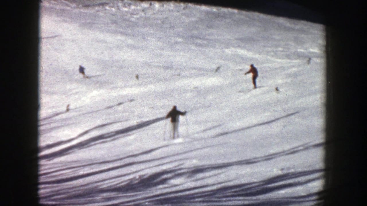 A skier glides downhill while other small figures cross the snowfield.