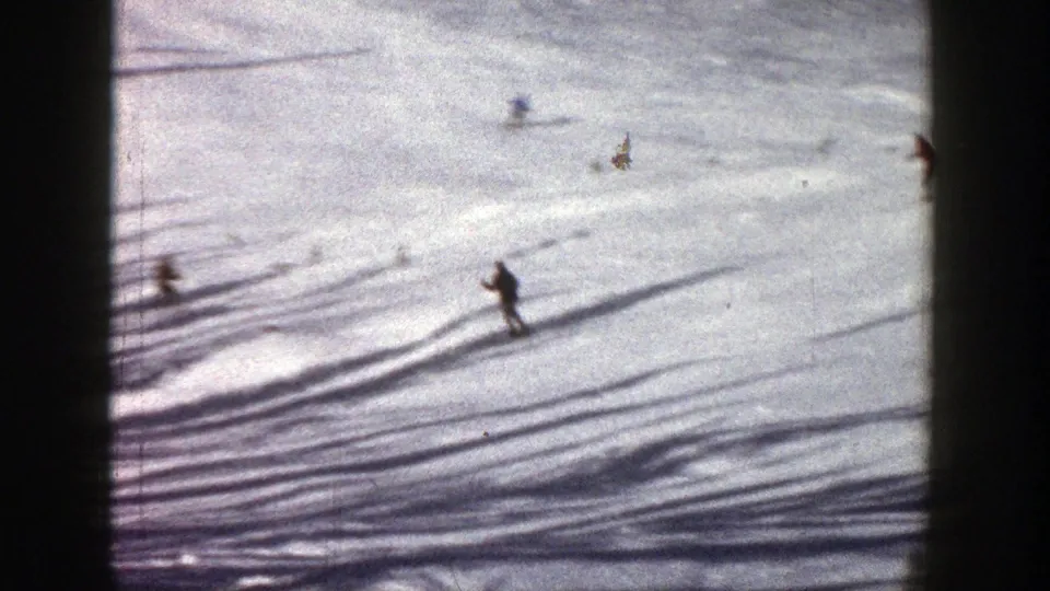 1961 Aspen 8mm frame showing scattered skiers on a broad snow-covered hillside, partly framed by dark film edges.