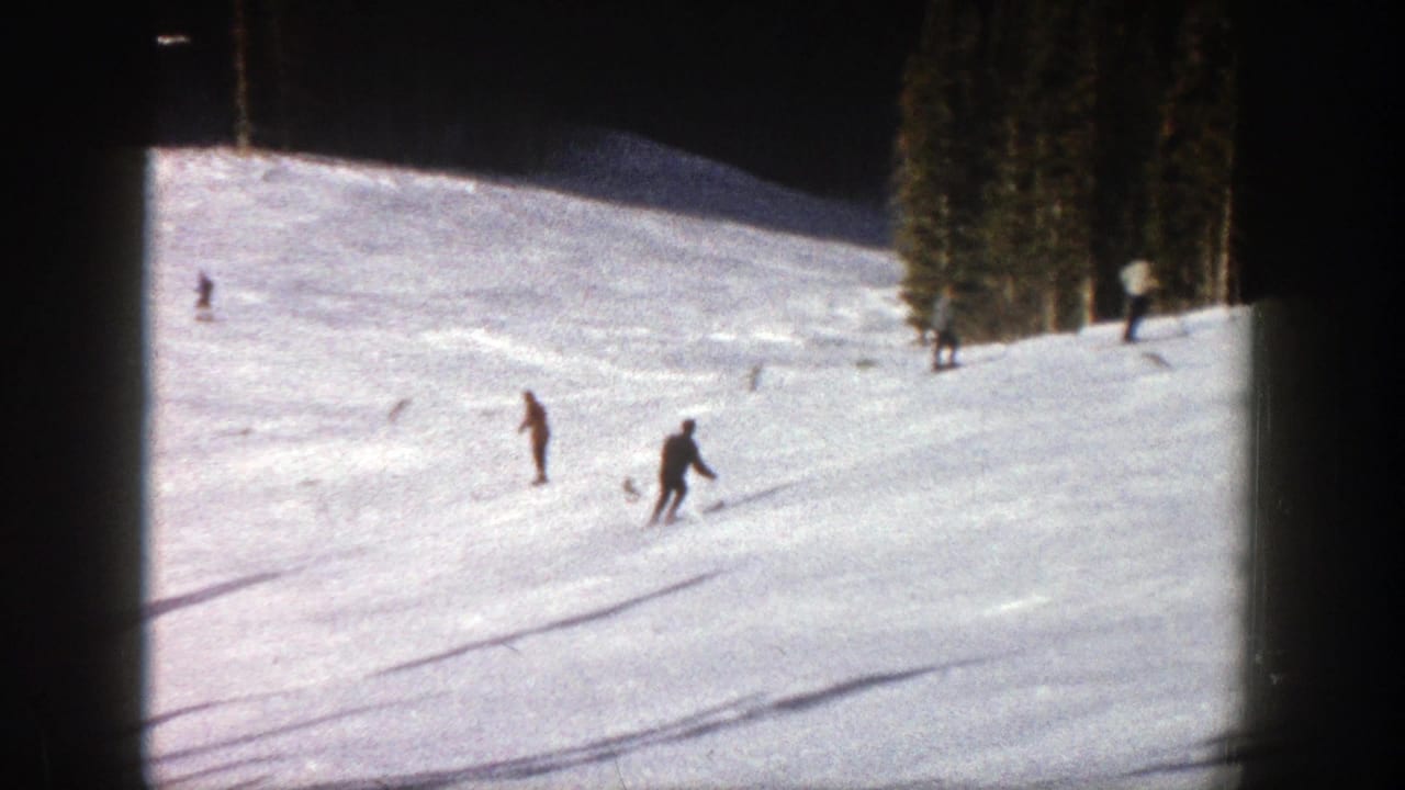 1961 Aspen home-movie frame showing distant skiers on a bright snowy slope with trees at the edge of the run.