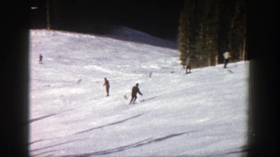1961 Aspen home-movie frame showing distant skiers on a bright snowy slope with trees at the edge of the run.