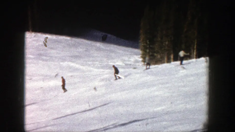 1961 Aspen frame with distant skiers on a snow-covered run, framed by dark film edges and evergreen trees to the right.