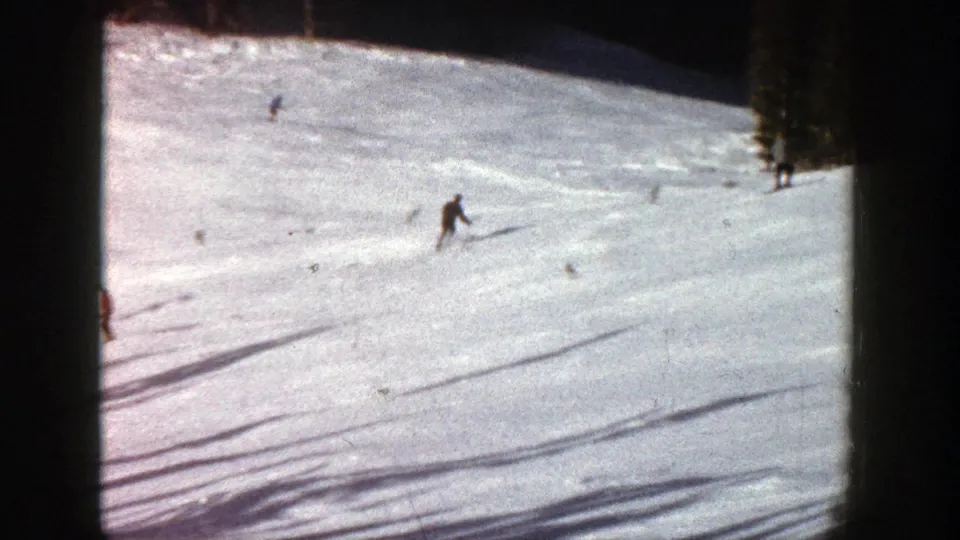1961 Aspen ski footage frame with one prominent skier descending an open snowfield and smaller figures higher on the slope.