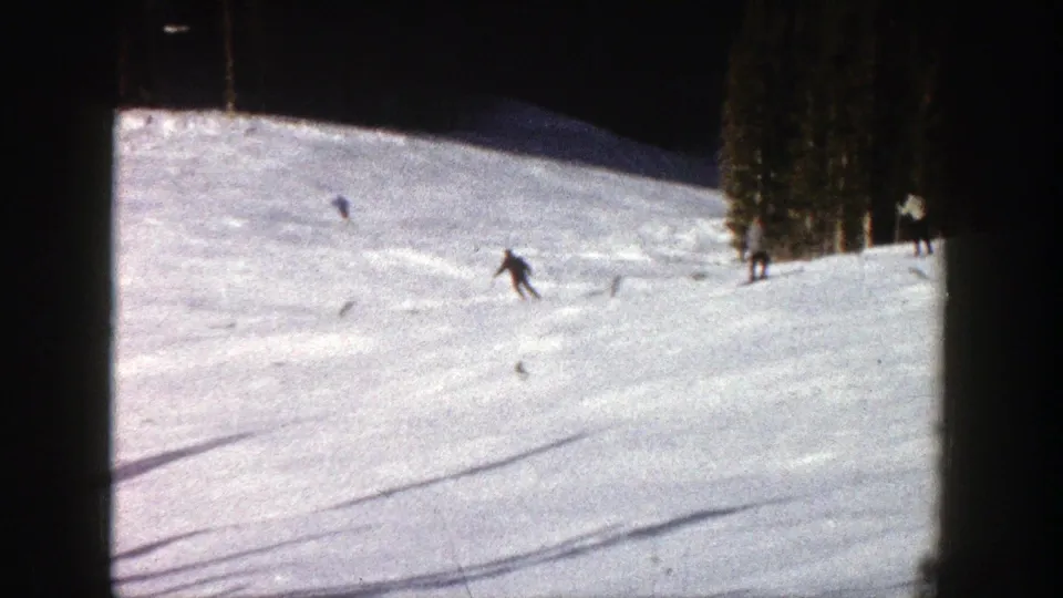 1961 Aspen 8mm frame showing skiers spaced across a wide slope, with trees on the right edge and soft film blur.