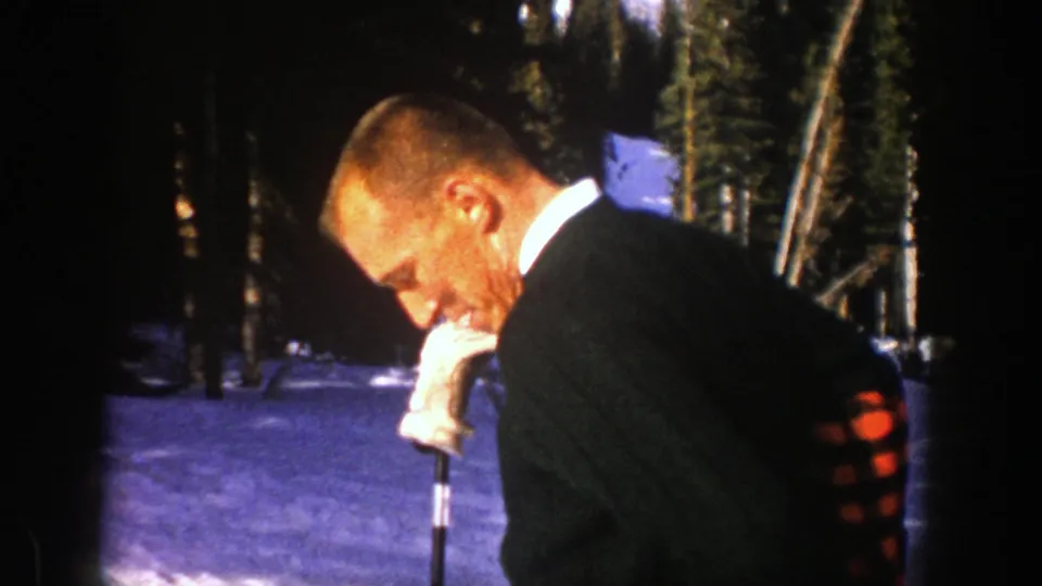 Man in a dark coat and white glove looks down near a ski pole in snowy Aspen woods, 1961.