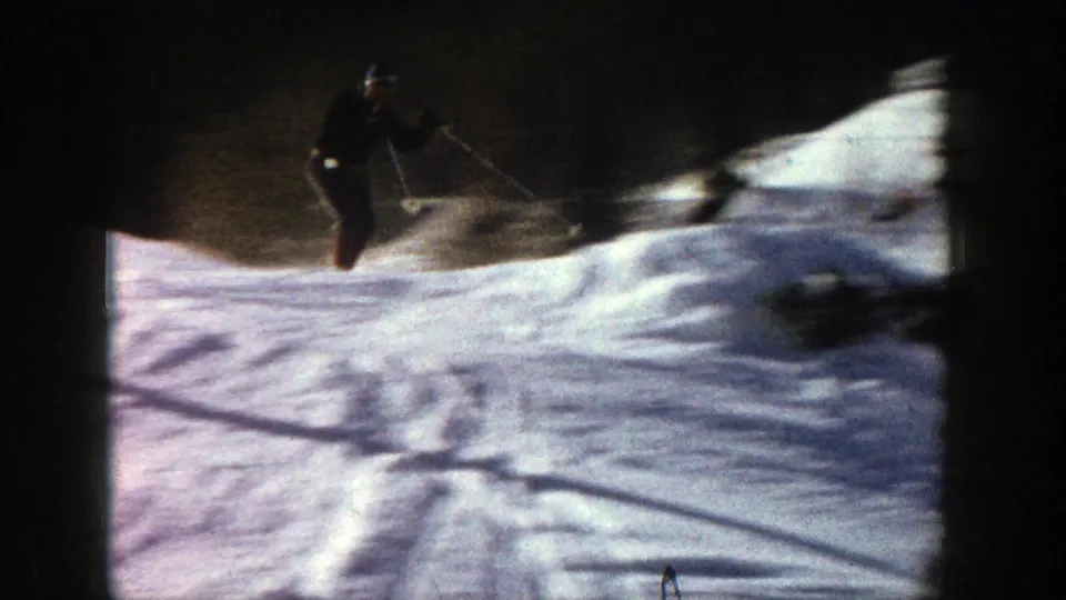 An adult skier descends a snow-covered Aspen slope with ski poles, framed by dark evergreen shadows and 8mm film edges.