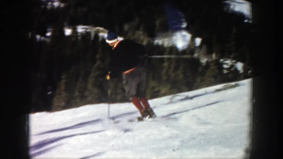 A skier descends a snowy Aspen slope with ski poles, framed by dark trees and strong sunlight in 1961 8mm footage.