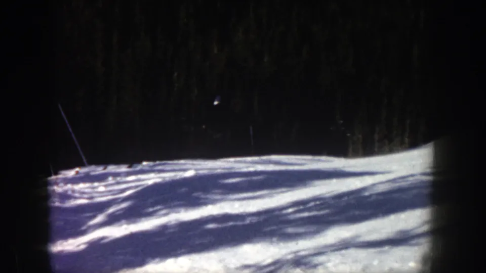 The Aspen ski slope is mostly empty in this frame, with bright snow, dark trees, and a partly visible skier or pole near the left edge.