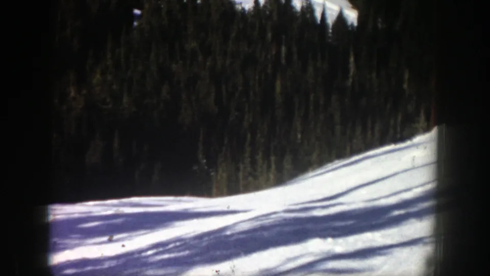 Aspen home-movie frame showing the snow-covered slope after the skier passes, with dark trees and shadows across the foreground.