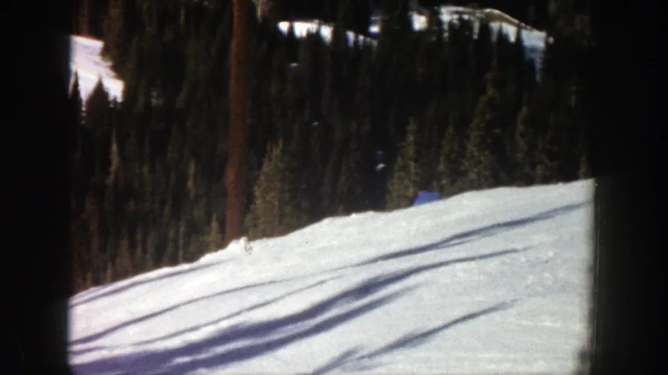 Near the end of the shot, the skier is mostly obscured by the snowy rise beneath tall Aspen evergreens.