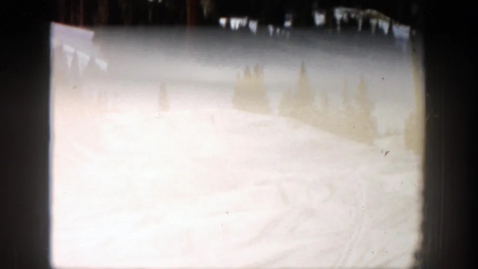 1961 Aspen home-movie frame of a bright snowy slope, heavily overexposed with faint evergreen trees and visible 8mm frame edges.