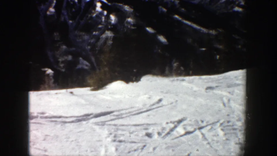 1961 Aspen ski-area footage showing marked snow tracks across a bright slope below dark trees.