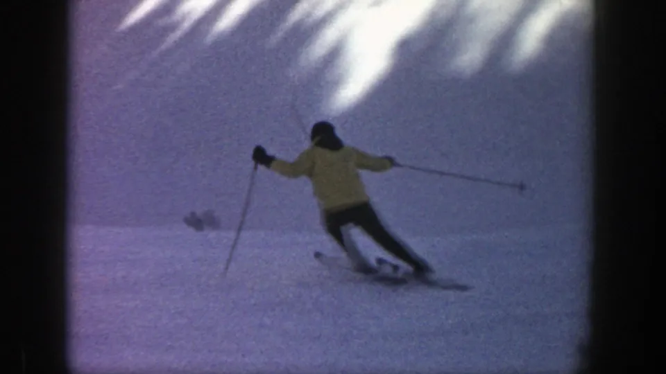 A skier viewed from behind turns downhill on a snowy Aspen slope, with pole plants and long skis visible.