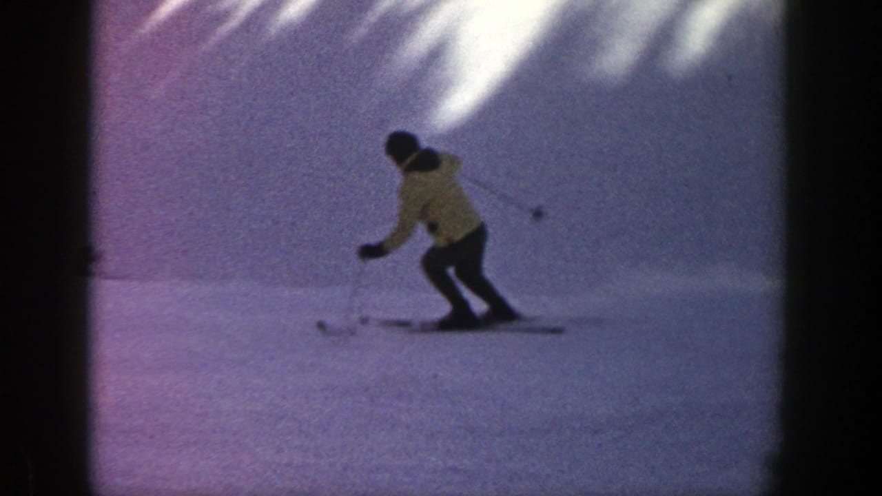 Skier in a yellow jacket descends a snowy slope with poles.
