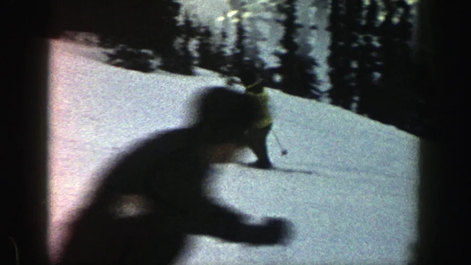 A close, motion-blurred skier crosses the frame on the Aspen slope, with snow and trees visible behind.