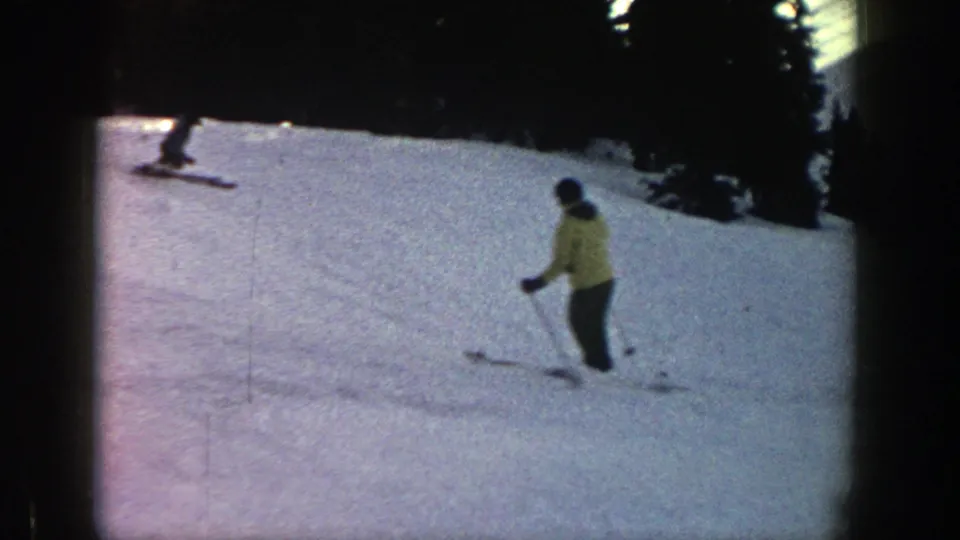 The yellow-jacketed skier continues downhill in Aspen, with another skier visible above on the snowy slope.