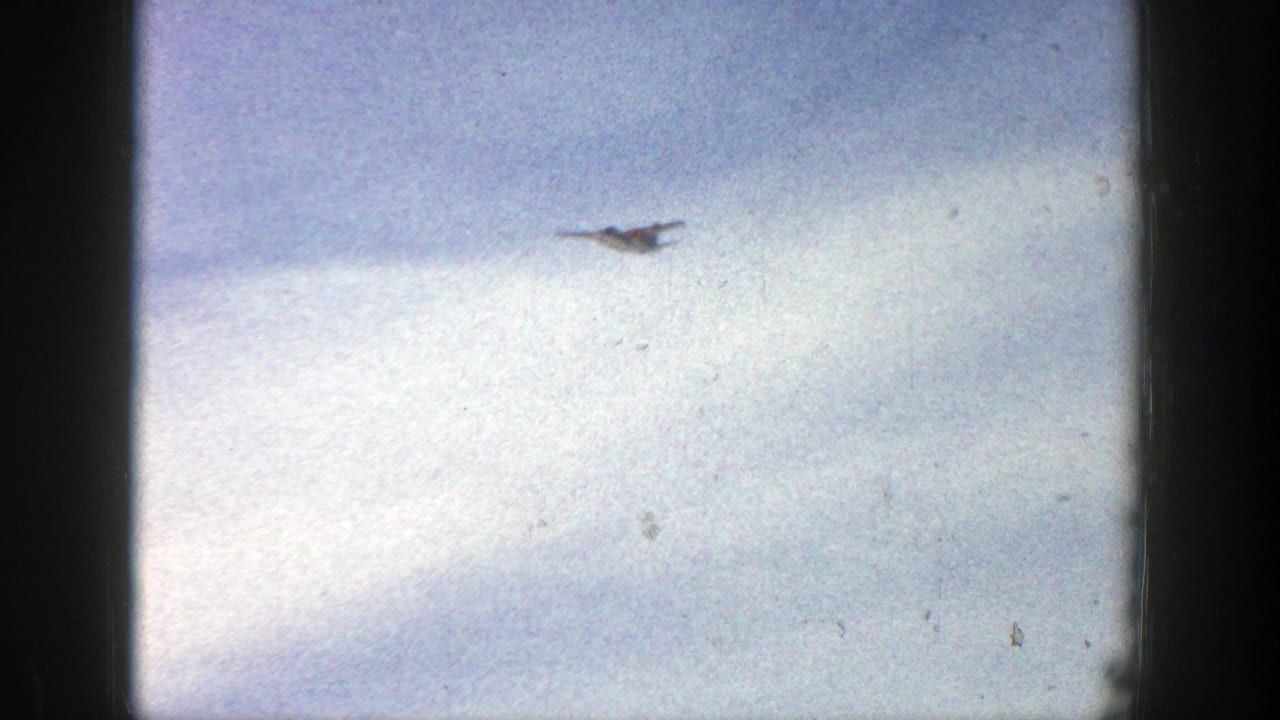 Small aircraft flying through pale clouds within a dark 8mm film frame.