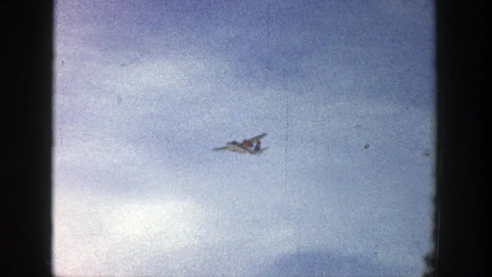 A small white aircraft is seen farther across the cloudy sky in this 1961 Aspen, Colorado 8mm frame.
