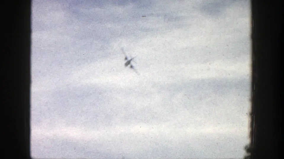 1961 Aspen frame with a small airplane banked in the sky, seen through grainy 8mm film texture.