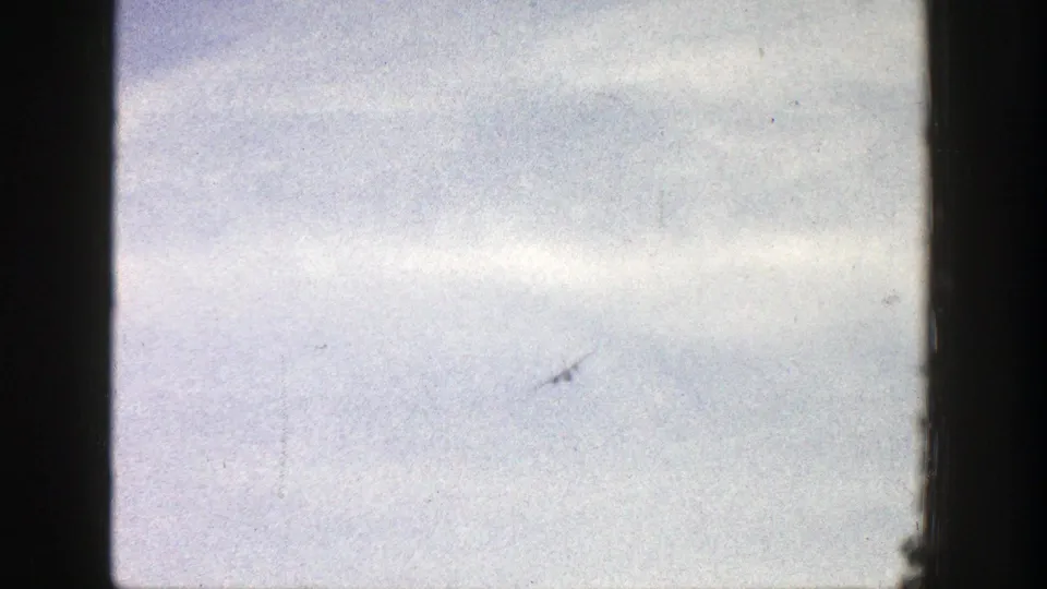 1961 Aspen frame with the airplane reduced to a small mark against a soft, clouded 8mm sky view.