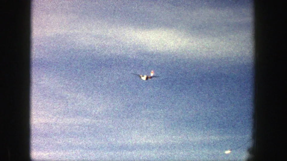 A small red and white plane is visible in the blue sky over Aspen, Colorado, captured on grainy 8mm film in 1961.