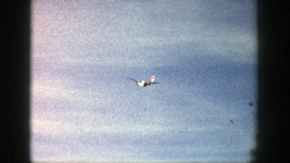 The small aircraft moves through the frame against a bright Aspen sky, with color fading and 8mm film texture apparent.
