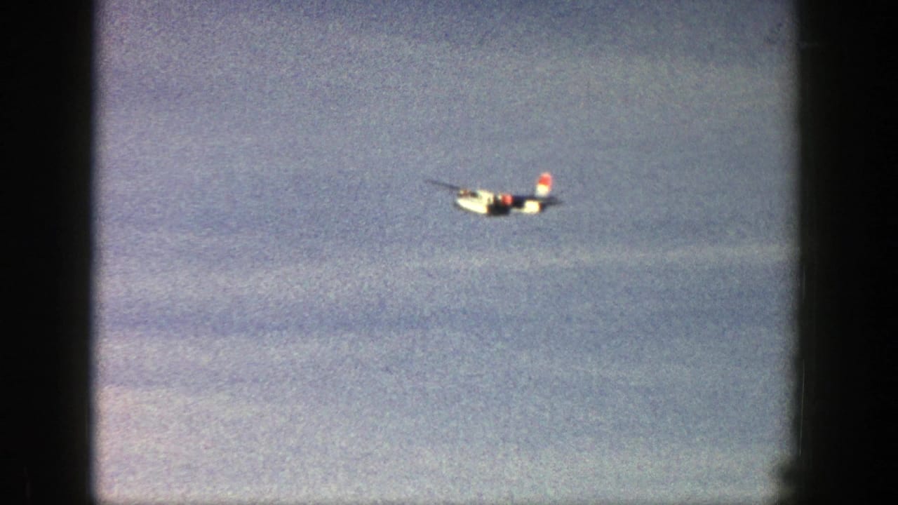 Small white aircraft in distant flight over a blue sky in 1961 Aspen, Colorado home-movie footage.