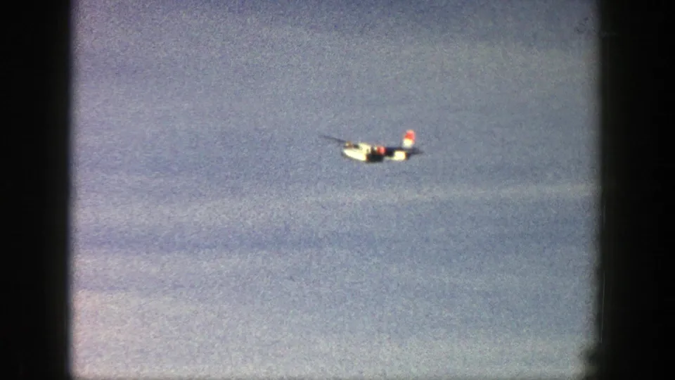 Small white aircraft in distant flight over a blue sky in 1961 Aspen, Colorado home-movie footage.