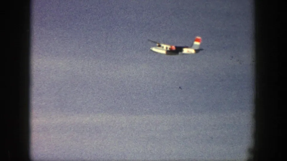 White plane with red and blue tail markings moving through the sky in Aspen, Colorado, 1961 footage.