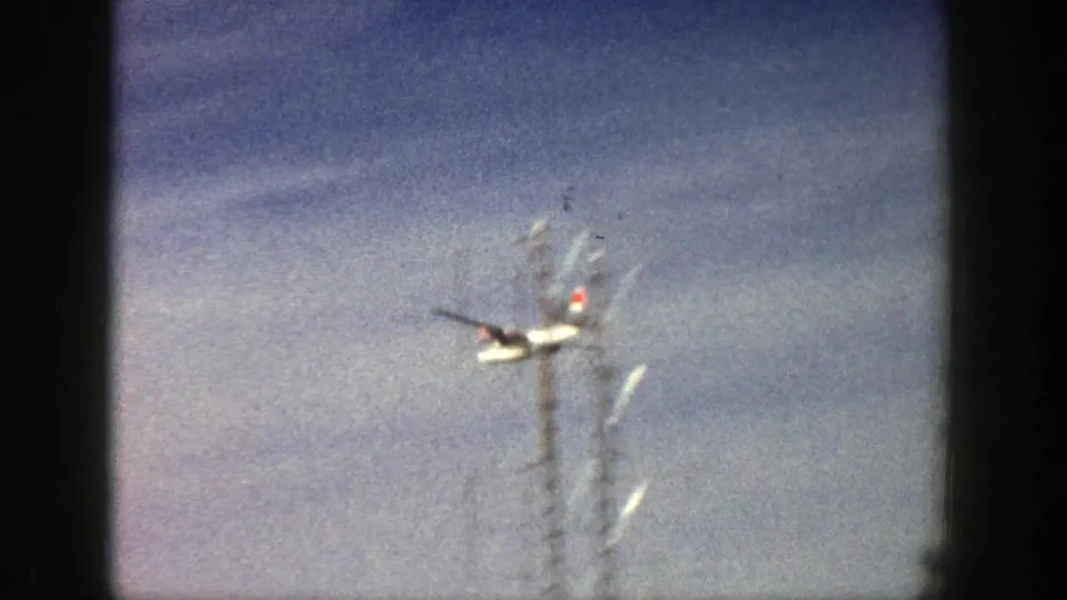 The aircraft continues across a pale winter sky, with visible 8mm film grain, scratches, and frame-edge shadowing.