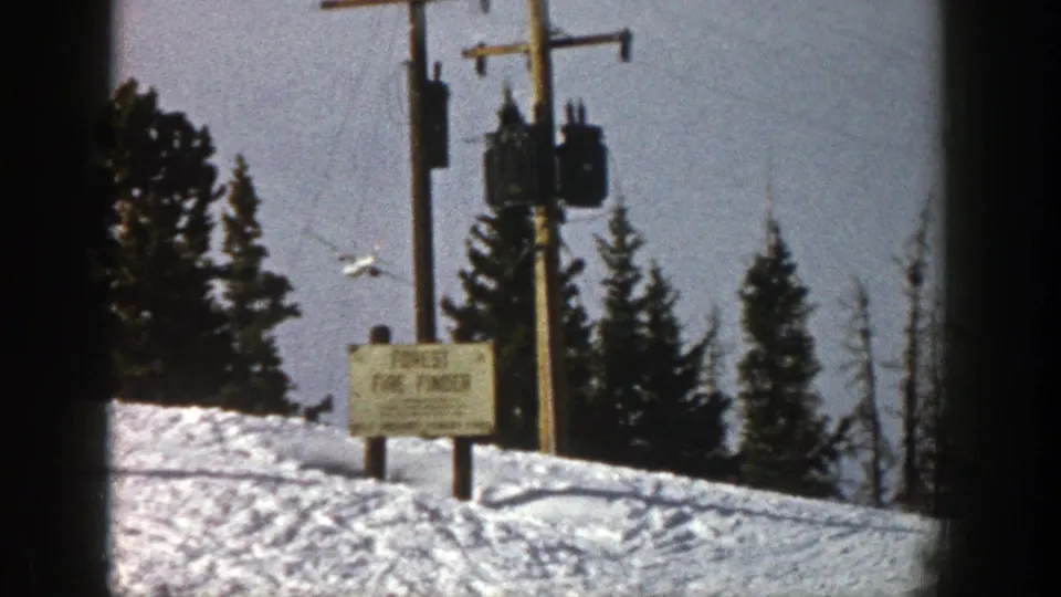 The airplane appears lower over a snowy Aspen, Colorado, landscape, with utility poles, evergreens, and a signpost in view.