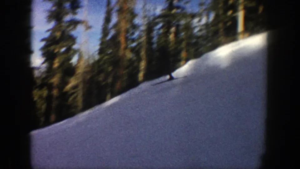 A wide snowy Aspen slope in 1961, with evergreen trees and a small distant skier near the edge of the run.