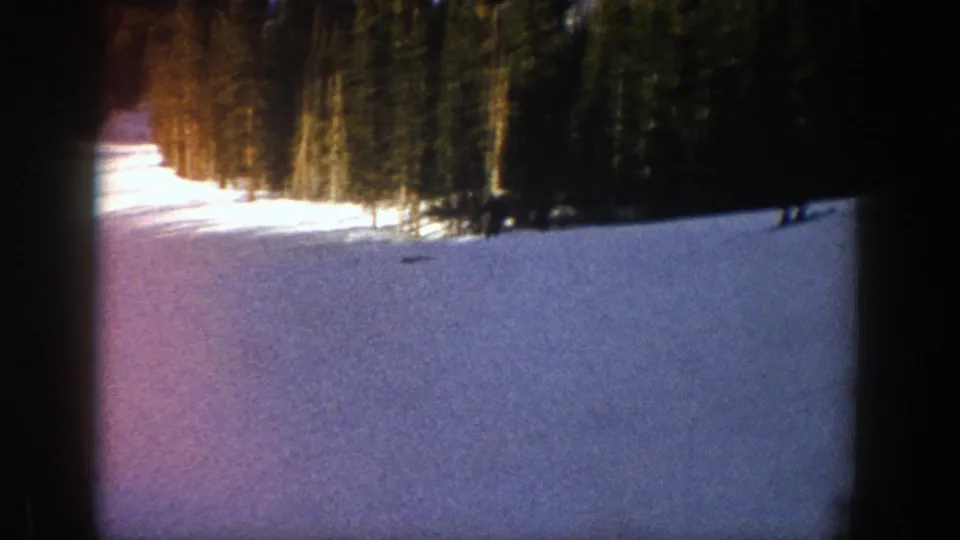 A wide view of an Aspen ski slope in 1961 shows snow, evergreen trees, shadowed areas, and small distant skiers.