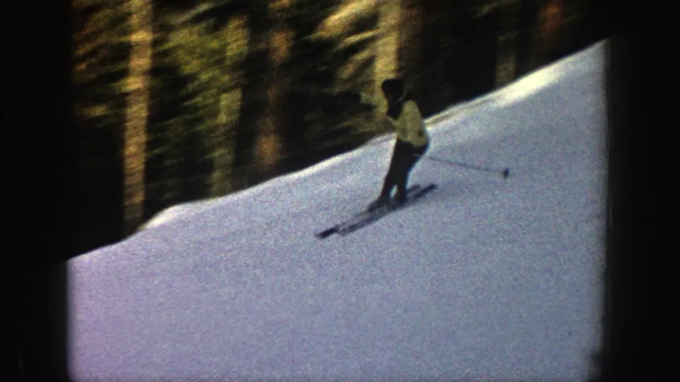 The skier traverses the snow in Aspen, Colorado, with a dark evergreen forest rising behind the slope.