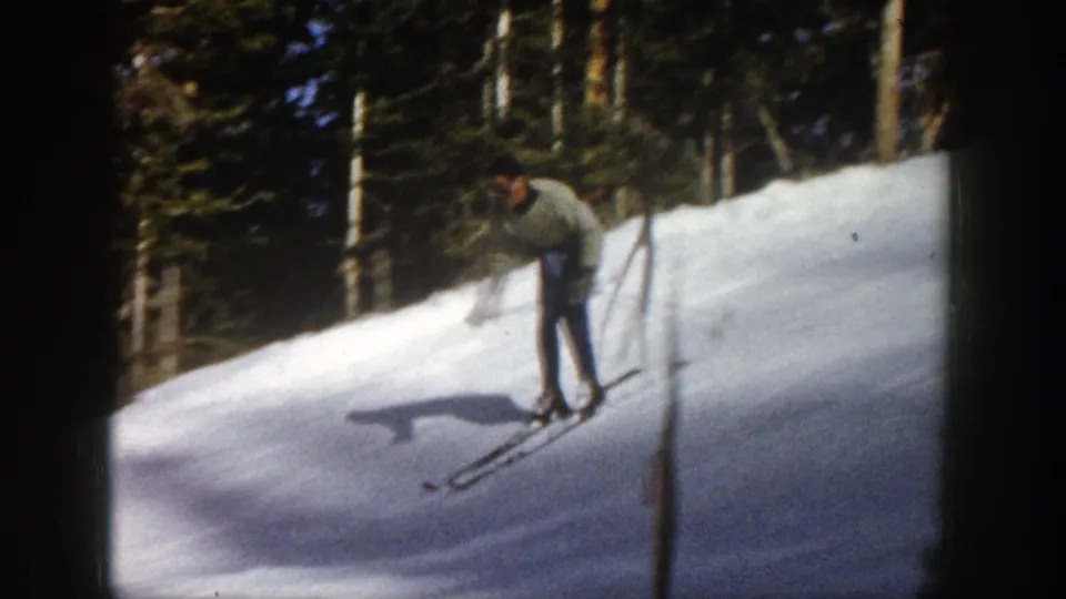 The skier moves downhill near a vertical trunk or pole, with long shadows across the 1961 Aspen snow.