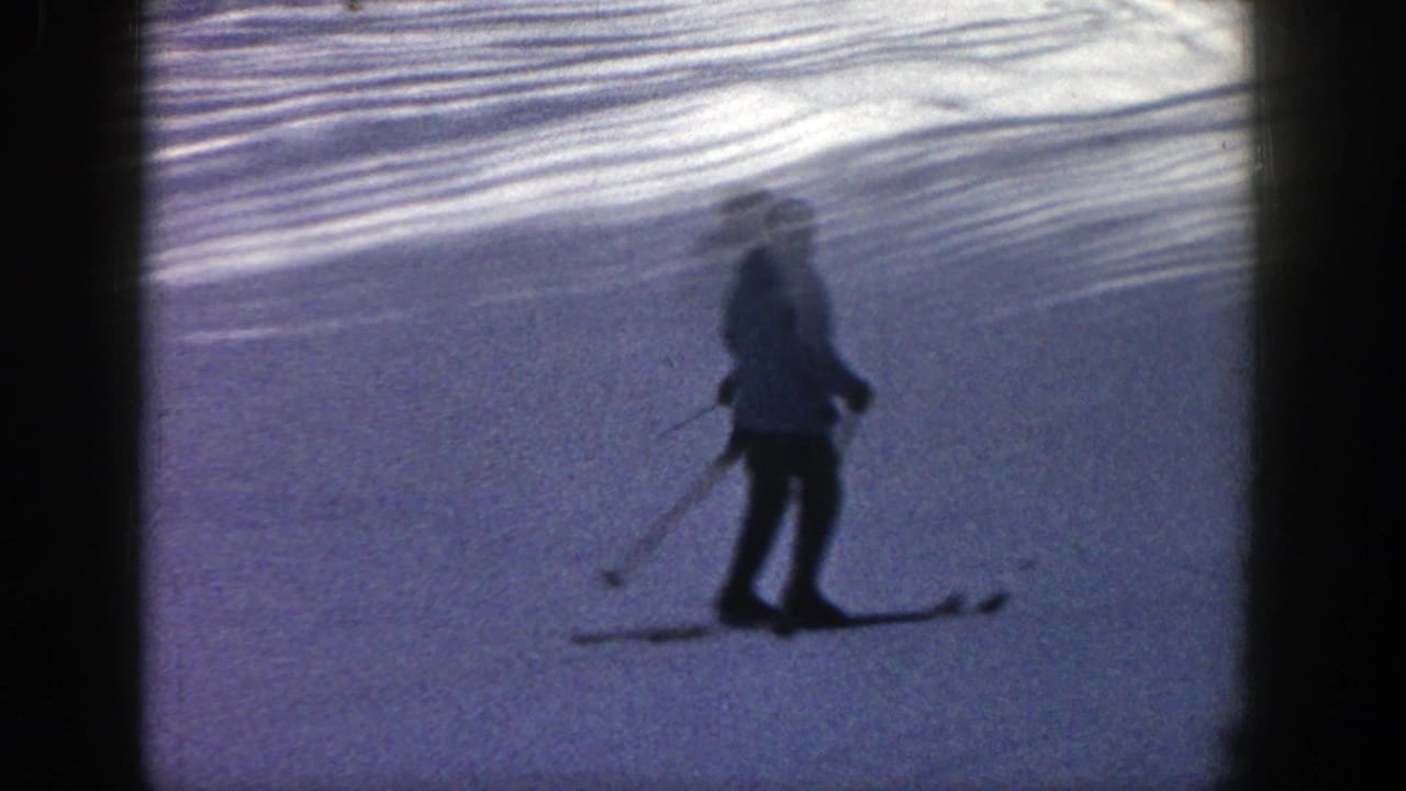 In Aspen, Colorado, 1961, a distant skier in dark pants appears on a bright snowy slope within a soft 8mm frame.